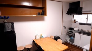 A compact kitchen with a microwave, stove, and sink. There is a wooden table with stools and a vase with flowers on the microwave. - GINTAKEI (Osaka)