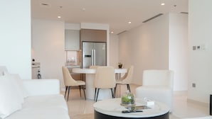 Una sala de estar moderna con un sofá blanco, una mesa de centro redonda y un comedor con una cocina al fondo.