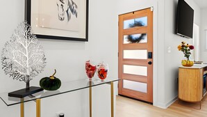 Un interior moderno con una mesa de vidrio que exhibe objetos decorativos, una puerta de madera y un televisor montado.