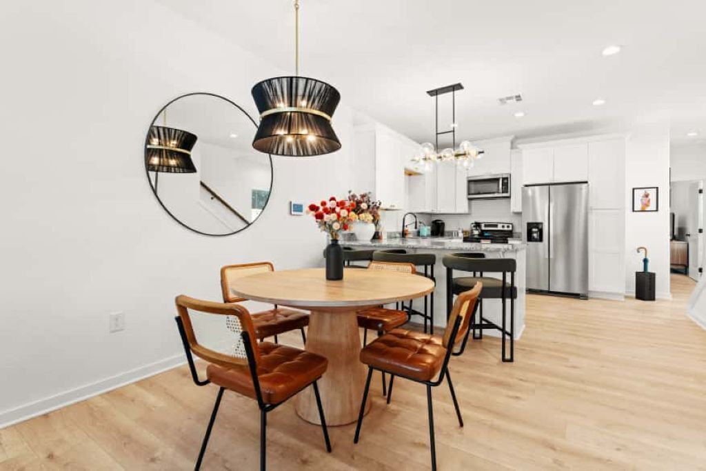 A modern kitchen with white cabinets, stainless steel appliances, and a round wooden dining table with leather chairs.
