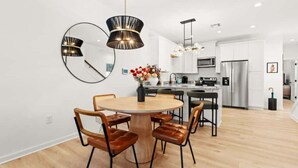 Una cocina moderna con armarios blancos, electrodomésticos de acero inoxidable y una mesa de madera redonda con sillas de cuero.