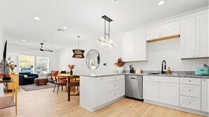 Una cocina moderna con armarios blancos, un comedor con mesa y sillas, y un amplio ventanal que proporciona luz natural.