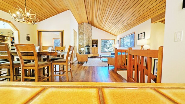 A spacious living area with a high ceiling and wooden beams, a stone fireplace, and large windows offering views of the outdoors. - Alpine 4 - SHARC, Hot Tub, A/C, Light & Bright! (Sunriver)