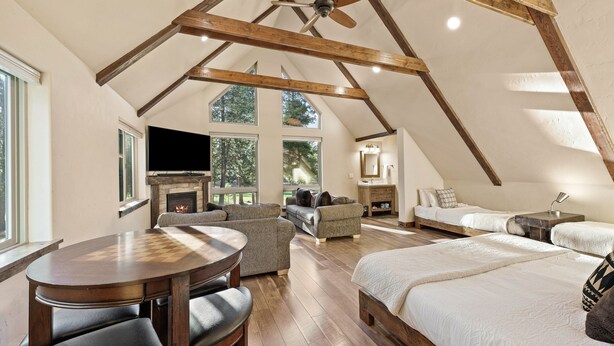 Une chambre spacieuse de style loft, dotée d’un grand lit, d’un plafond en bois, d’une cheminée et d’un téléviseur.