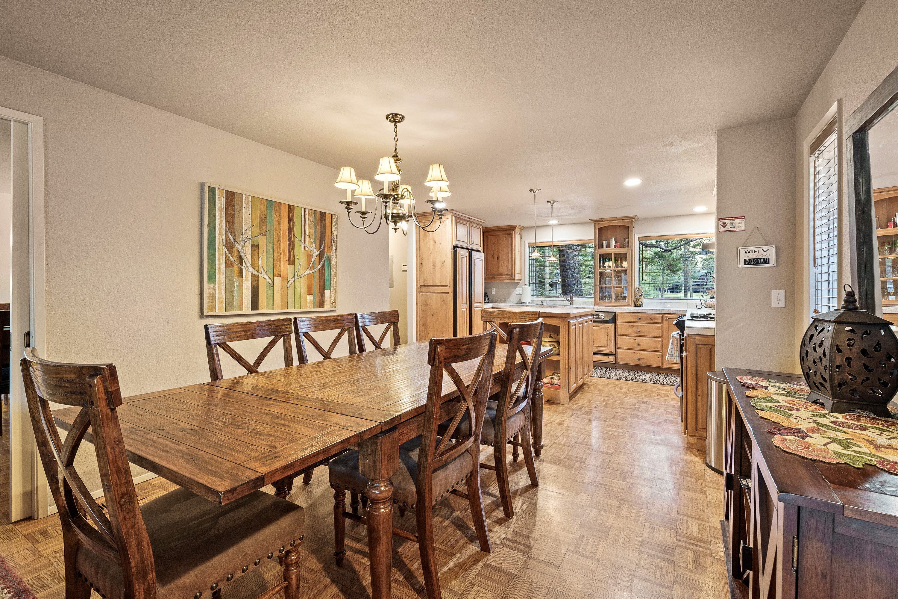 Un vaste espace dédié à la salle à manger, avec une table et des chaises en bois, un lustre, et une vue sur la cuisine et l’extérieur.