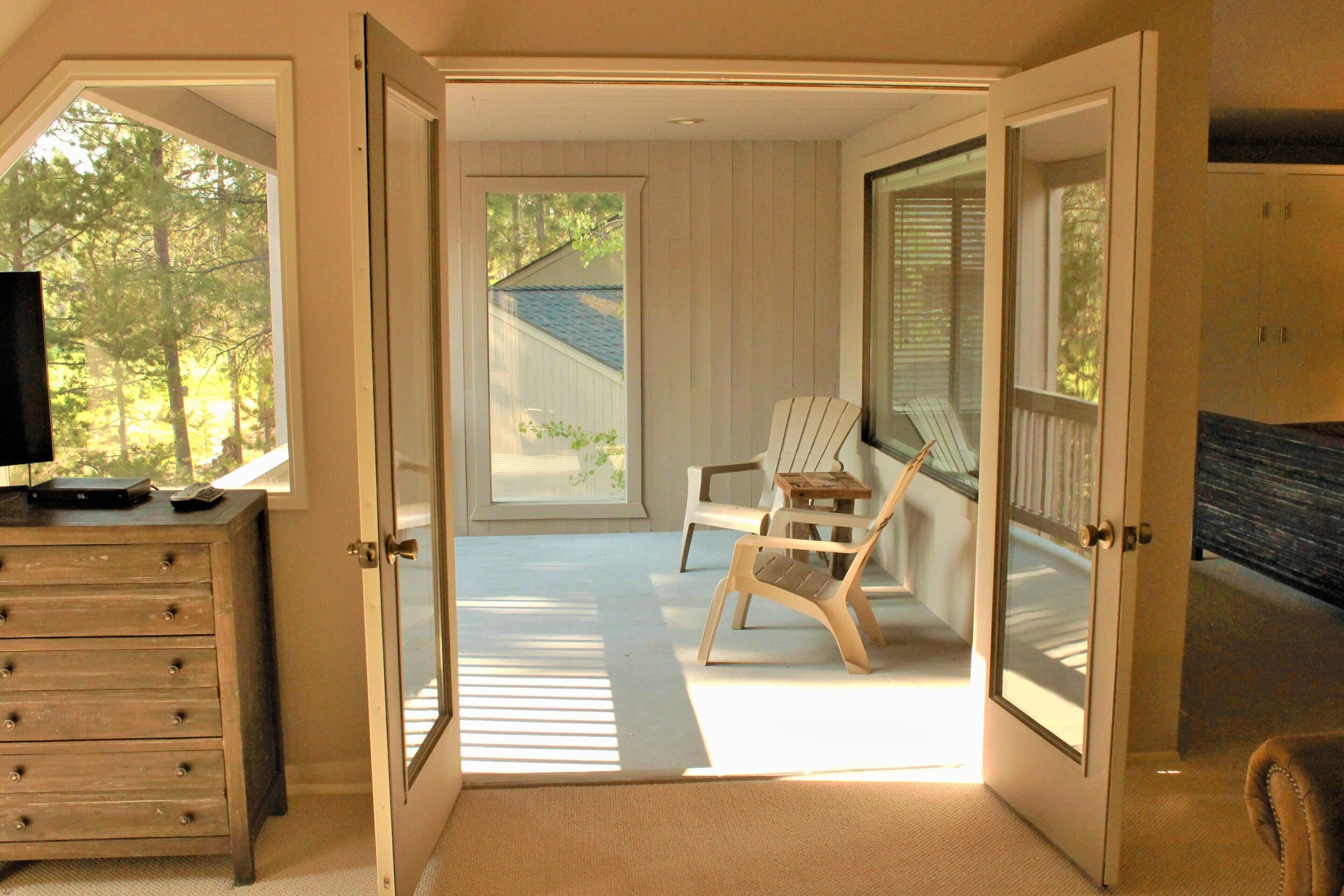 An open door leading to a porch with a wooden chair, a small table, and a dresser with a television.