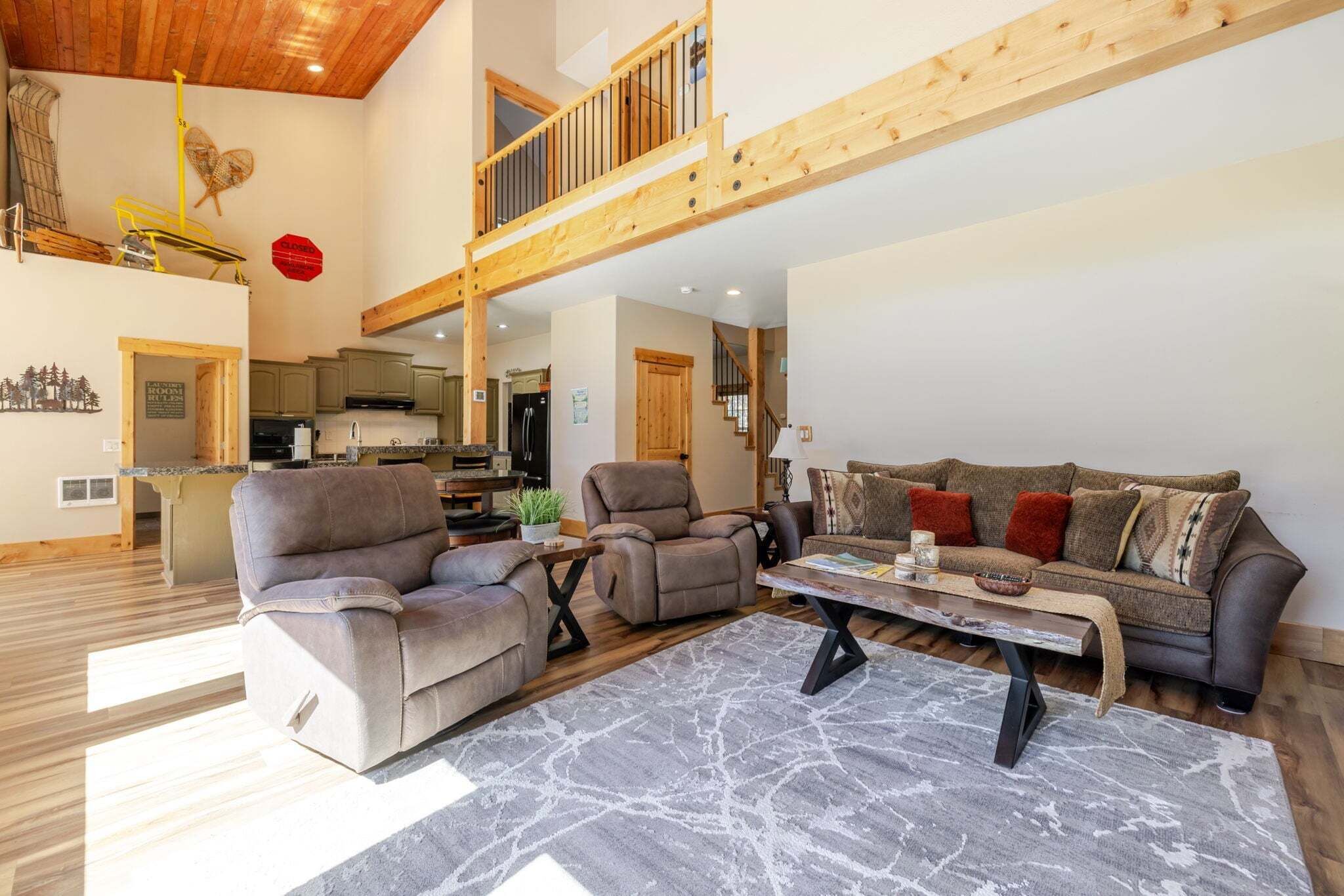 A spacious living area with a high ceiling, a wooden balcony, a sofa set, and a dining table.