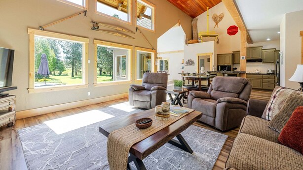 A spacious living area with a high ceiling, wooden beams, and large windows offering a view of the outdoors. - Aspen Place - River Access, Ping Pong, Gorgeous Home & Location (Three Rivers)