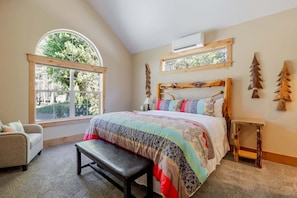 Un dormitorio con una cama grande, un banco, una silla, un ventanal y una mesita.