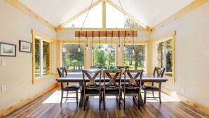 A dining area with a wooden table and chairs, large windows, and a high ceiling with exposed beams. - Aspen Place - River Access, Ping Pong, Gorgeous Home & Location (Three Rivers)