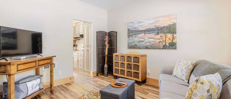 A living room with a TV, a sofa, a coffee table, a patterned rug, and a painting of a landscape.