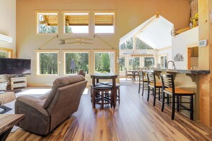 A spacious living area with a large window, a fireplace, and a dining area with wooden chairs and a table.