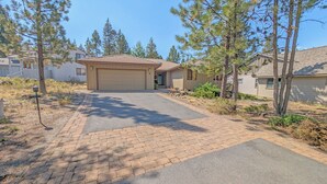 A residential property with a paved driveway leading to a garage, surrounded by pine trees and a landscaped garden. - Big Leaf 4 - SHARC, Hot Tub, Ping Pong (Sunriver)