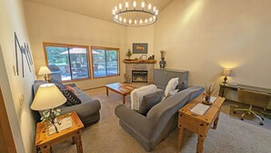 A living room with a fireplace, a sofa, a coffee table, and a chandelier. - Big Leaf 4 - SHARC, Hot Tub, Ping Pong (Sunriver)