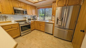 A kitchen with wooden cabinets, stainless steel appliances, a microwave, oven, dishwasher, and a refrigerator. - Big Leaf 4 - SHARC, Hot Tub, Ping Pong (Sunriver)
