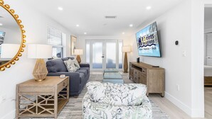A modern living room with a sofa, ottoman, and a TV on the wall. - Plunge into Joy & Sun at Siesta Key Coastal Gem - Aloha Kai #60 (Siesta Key)