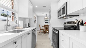 A modern kitchen with white cabinetry, a built-in oven, and a microwave. There is a dining area with a wooden table and chairs. - Plunge into Joy & Sun at Siesta Key Coastal Gem - Aloha Kai #60 (Siesta Key)