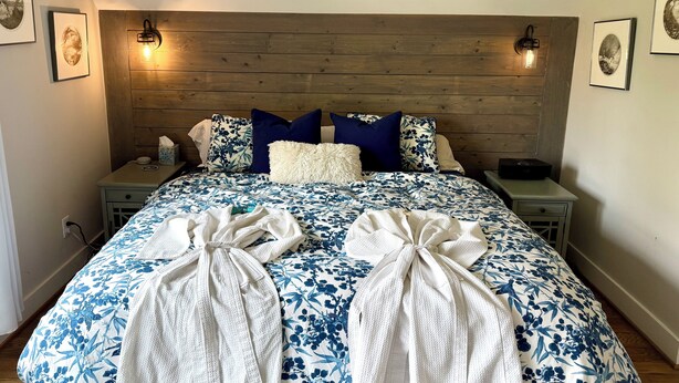 A neatly made bed with floral bedding, two bedside tables with lamps, and towels tied on the bed. - Capital Cottage-Merrimon-Wynne, Garage, Walkable! (Raleigh)
