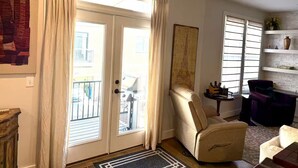 A living room with a beige armchair, a dark-colored sofa, a small table, and a decorative piece on the wall. - Capital Cottage-Merrimon-Wynne, Garage, Walkable! (Raleigh)