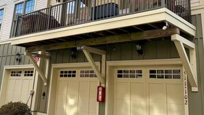 A two-story building with a balcony, two garage doors, and a small garden area. - Capital Cottage-Merrimon-Wynne, Garage, Walkable! (Raleigh)