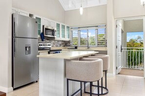 A modern kitchen with stainless steel appliances, a large island with bar stools, and a view of the outdoors through a window. - 3rd Floor Condo Richmond Estate Beach Access Pool (St. Ann's Bay)
