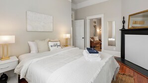 A bedroom with a large bed, bedside lamps, a mirror, and a door leading to another room.