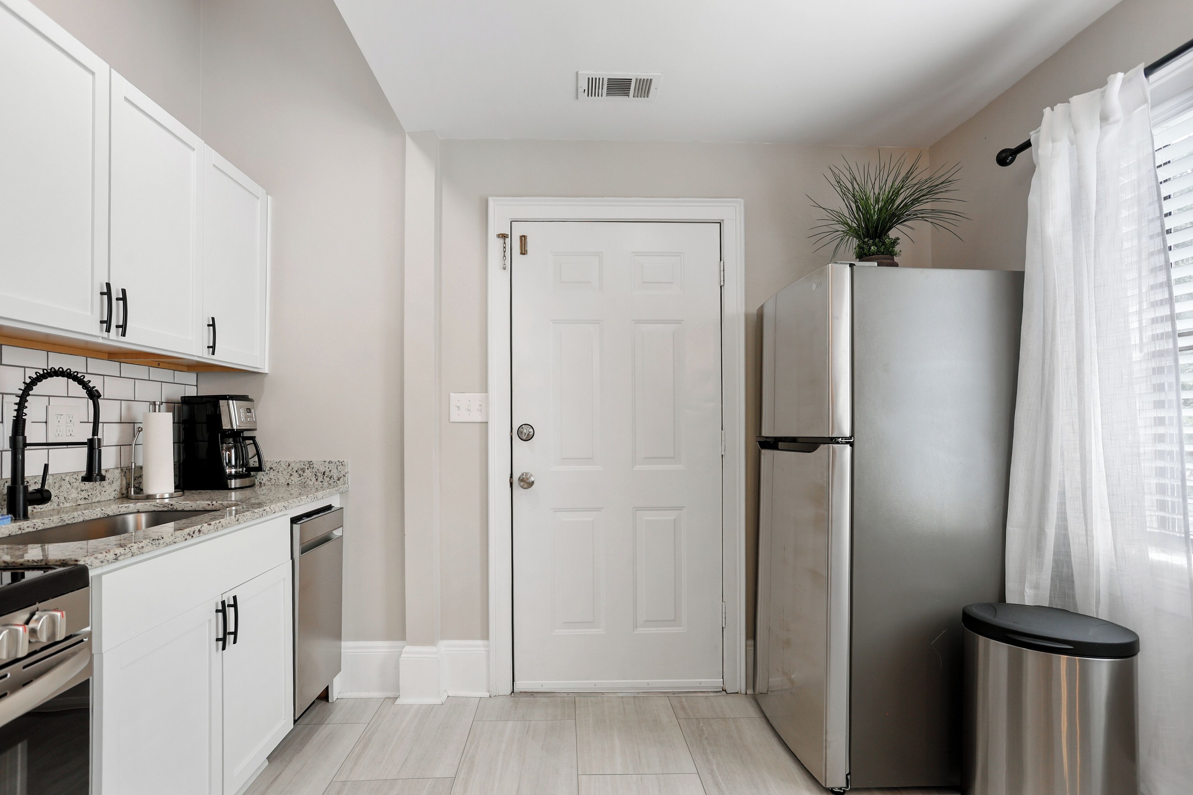 A compact kitchen with white cabinets, a stainless steel refrigerator, a coffee maker, and a trash can.