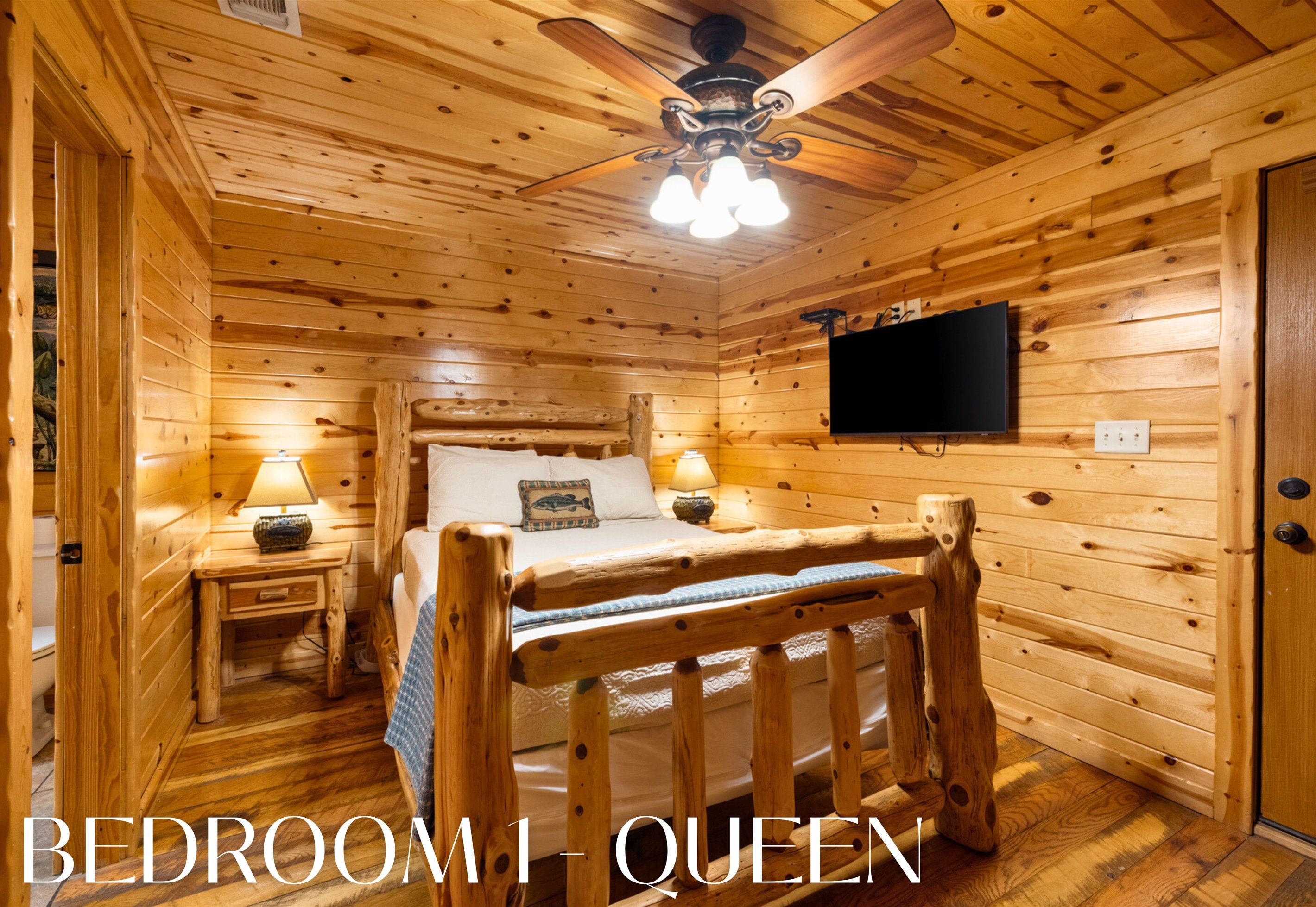 A cozy wooden bedroom with a bed, a ceiling fan, and a mounted TV.