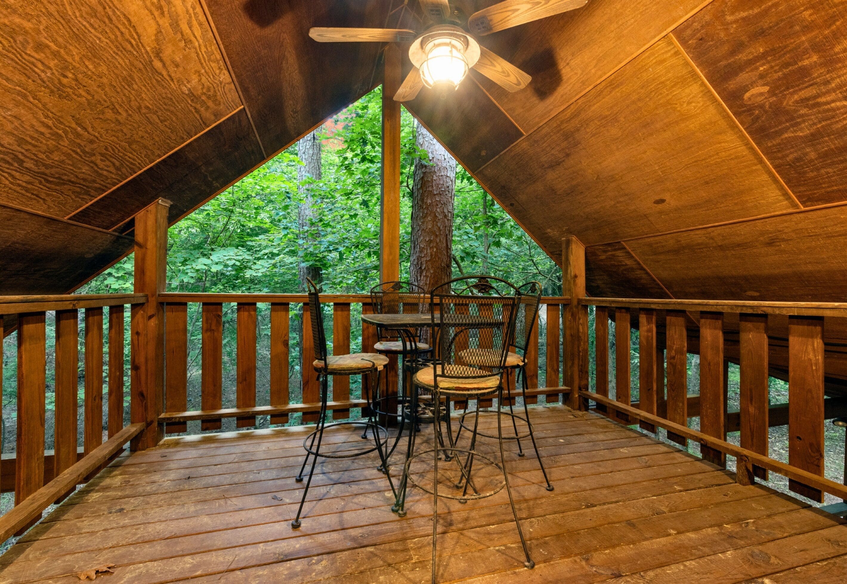 Een kamer in zolderstijl met een houten terras, een plafondventilator en een tafel met stoelen.