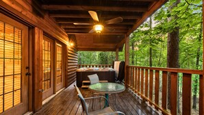 A wooden deck with a glass table and chairs, a hot tub, and a view of the forest.