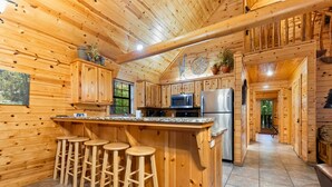 A wooden cabin kitchen with a bar area, stools, a refrigerator, and a microwave.