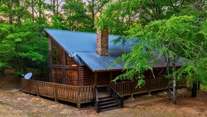 A cabin with a metal roof, wooden deck, and a chimney.