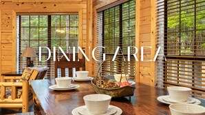A dining area with wooden walls, large windows, and a table set with white plates and bowls.