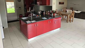 A modern kitchen with red cabinetry, a central island, and a dining area with wooden furniture.