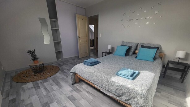 A modern bedroom with a large bed, a small side table, a nightstand, a potted plant, and a wardrobe.