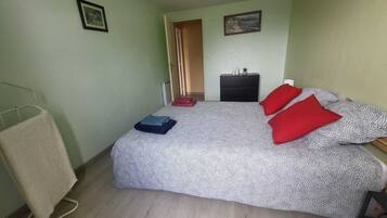 Ein kleiner, ordentlich eingerichteter Schlafzimmer mit Bett, Nachttisch, Stuhl, Heizkörper und einer Tür zu einem anderen Raum.