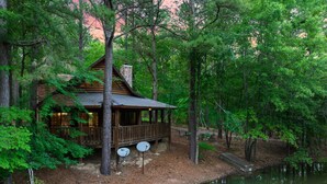 Eine Hütte mit einer Terrasse, umgeben von dichtem Wald und einem Gewässer.