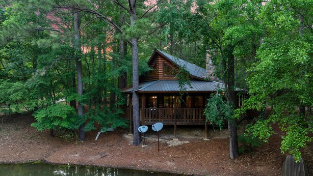 Eine Holzhütte mit einer Holzterrasse und einem Steg, der in einen See führt, umgeben von dichtem Wald.