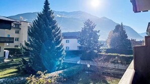 A residential area with a mountain in the background, a white building with blue shutters, and a large evergreen tree in the foreground. - Lovely apartment for 5 people with WIFI, TV and pets allowed (Bormio)