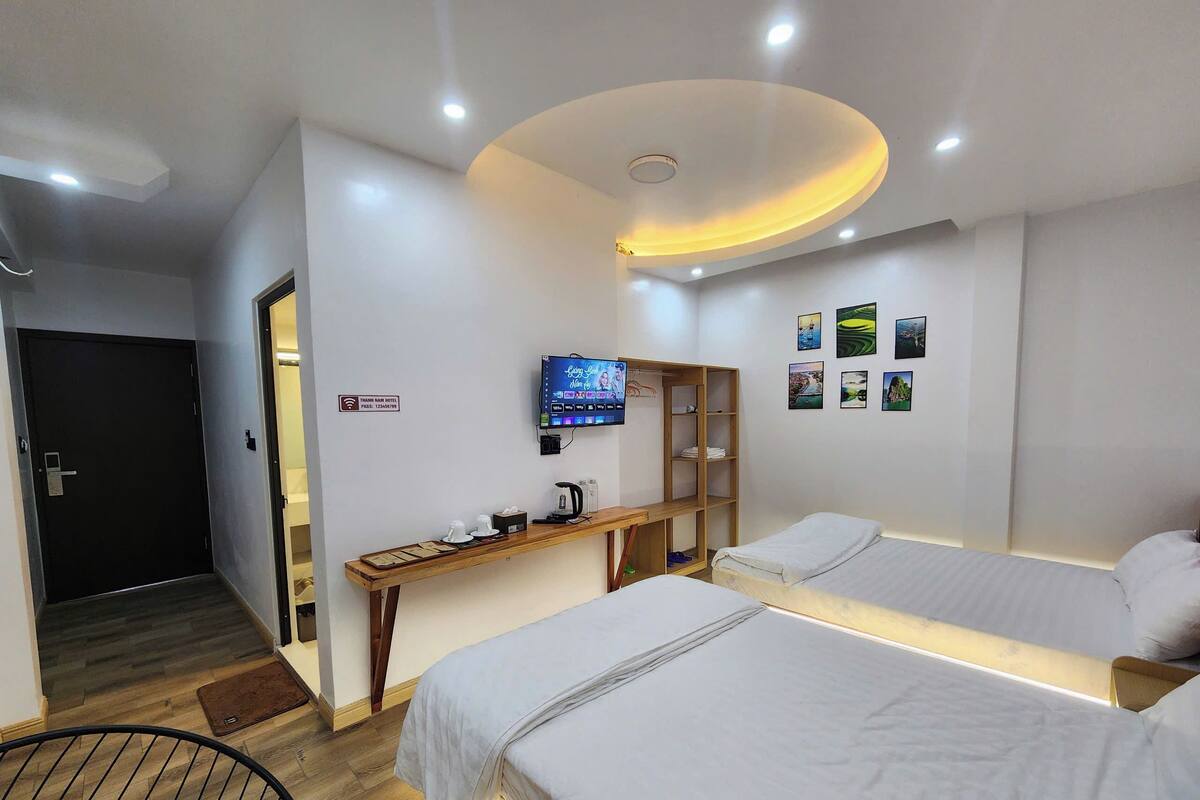 A hotel room with two beds, a desk with a television, and a bookshelf.