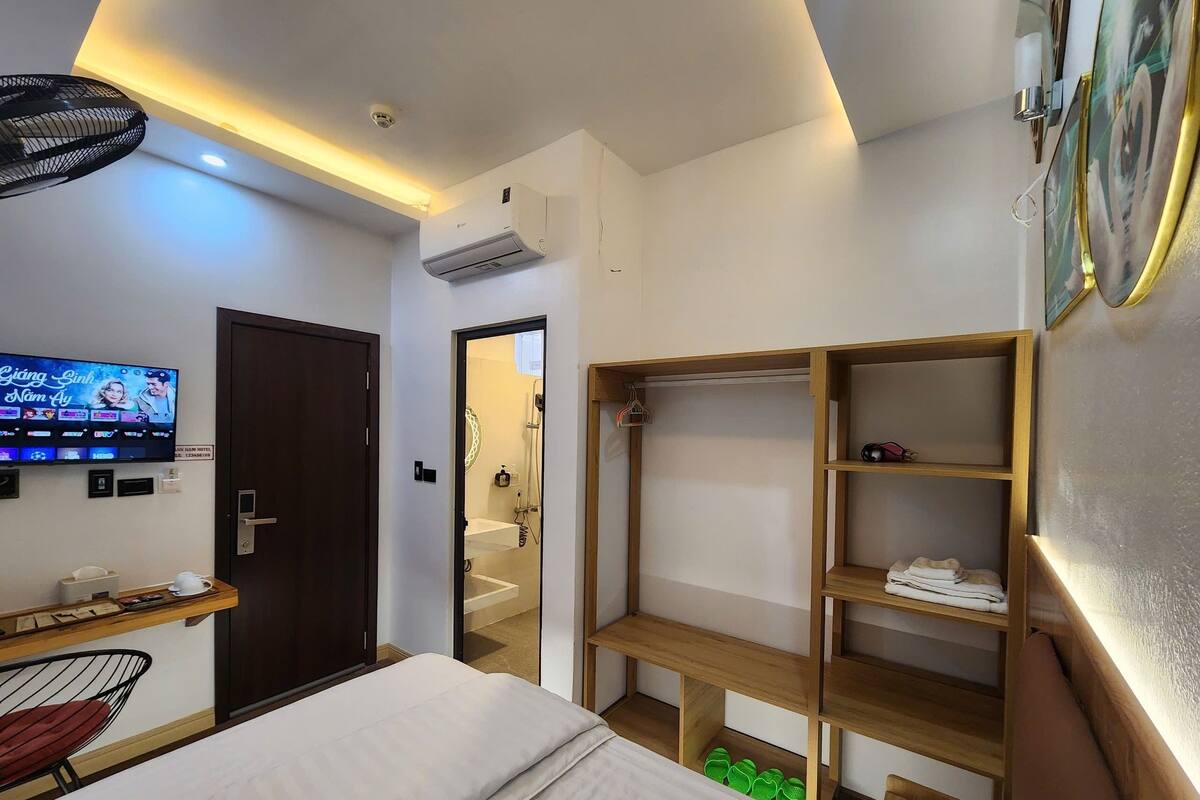 A hotel room with a bed, a TV, a desk, a wardrobe, and a shower area.