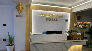 Un mostrador de recepción con frente de mármol y detalles de madera. El área de recepción tiene un cartel que dice "THANH NAM HOTEL".