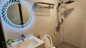 Un baño moderno con un espejo redondo, un lavabo blanco, un inodoro y una ducha.