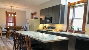 A modern kitchen with a marble island, wooden chairs, a built-in oven, and a window with curtains.