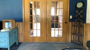 A room with a wooden door with glass panels, a blue wall, a small wooden shelf with books, and a metal decorative piece.