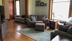 A living room with a wooden floor, a brown sofa, a grey armchair, and a television on a wooden cabinet.