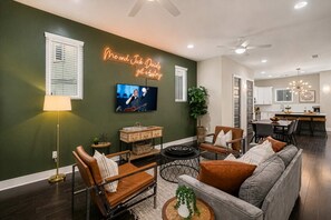 Een moderne woonkamer met een televisie, leren fauteuils, een bank en een neonbord.