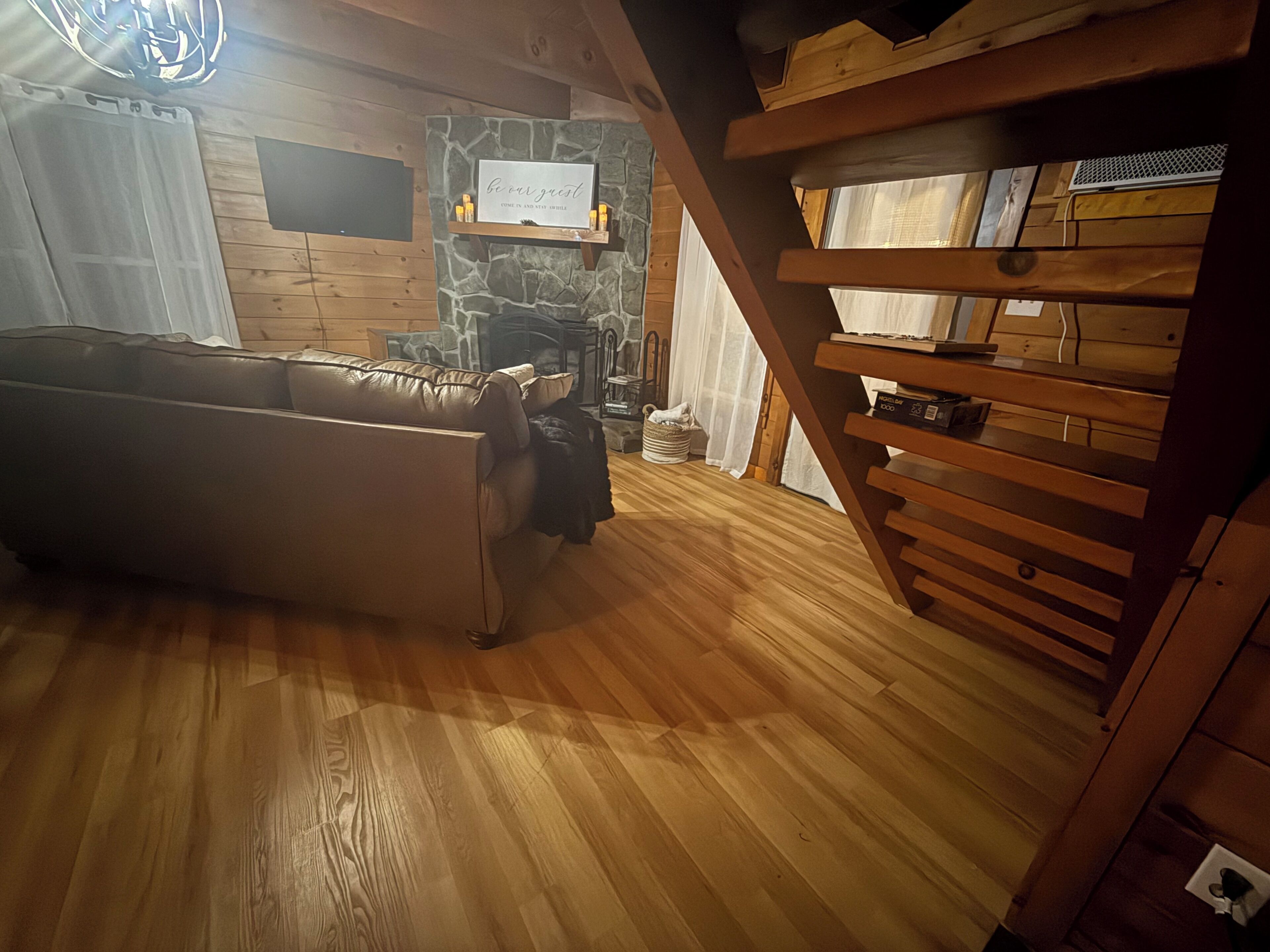 Una sala de estar acogedora con piso de madera, un sofá de cuero, una chimenea de piedra y una escalera de madera.