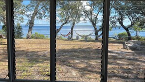 Vista por una ventana con una hamaca, un banco y un área verde que lleva a una masa de agua.