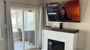 Una sala de estar con televisión de pantalla plana, ventilador de techo, chimenea y puerta corrediza de vidrio que da a un balcón.